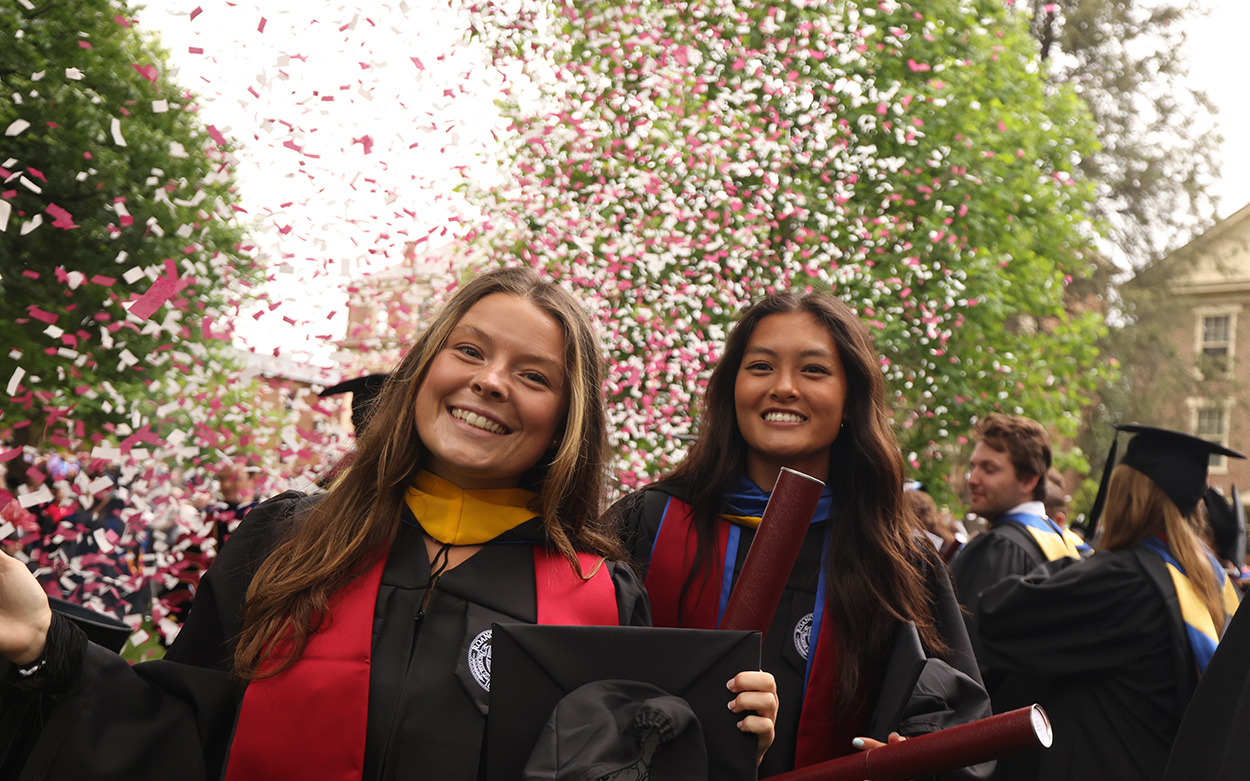 Two students smile against a backdrop of falling, multi-colored confetti