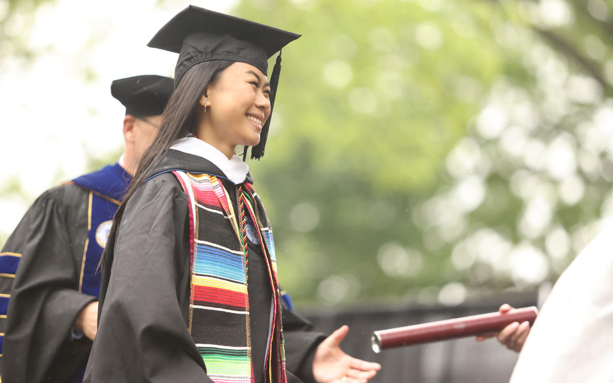 A student smiles while accepting her diploma on stage