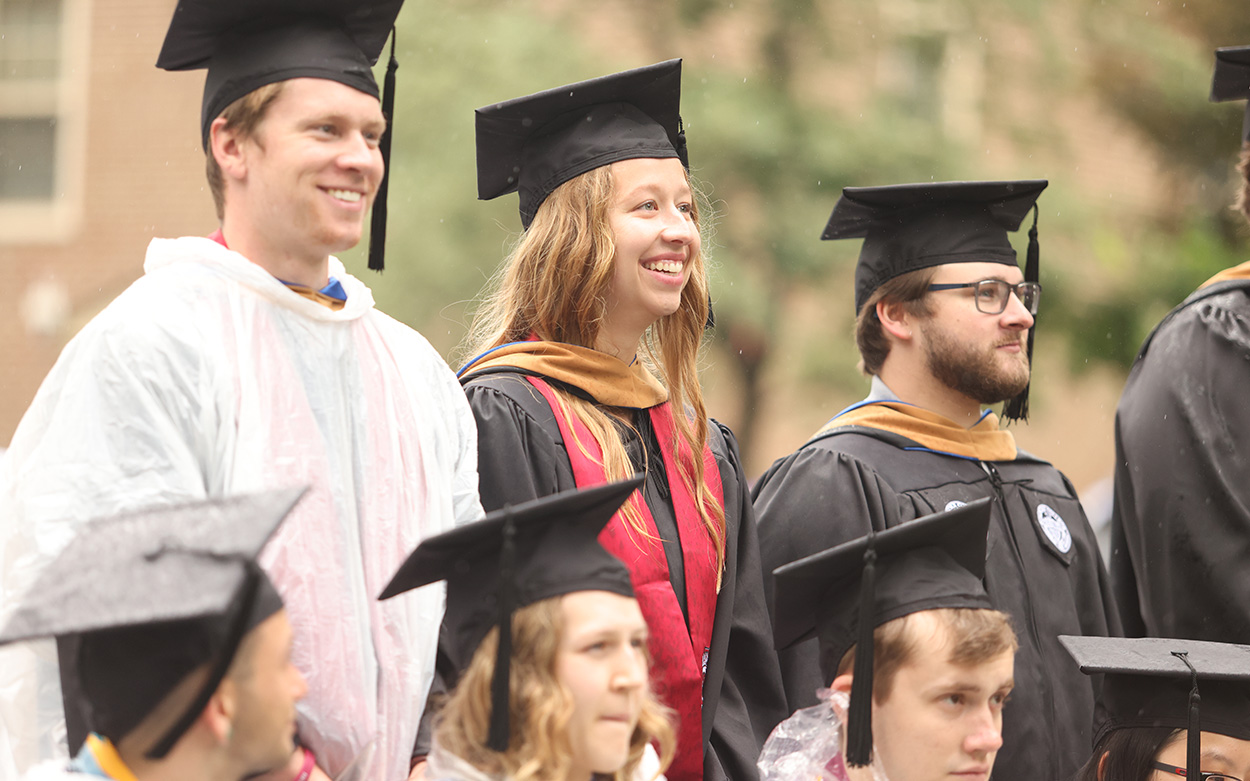 MBA gradautes in commencement caps smile while standing to be applauded by the crowd