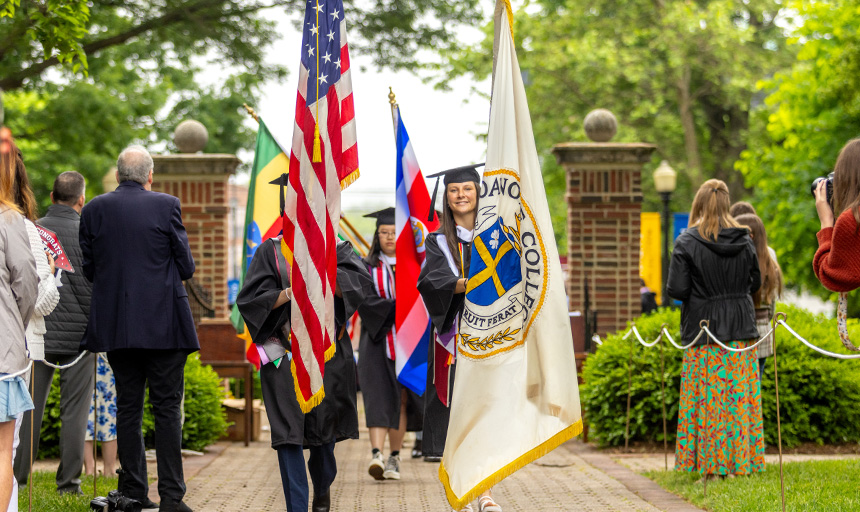 Two students, one carrying the Roanoke College flag and one carrying the U.S. flag, lead the ceremonial procession to start Commencement