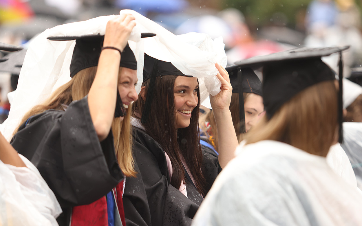 Two students smile while lifting a poncho overhead to use as a shared umbrella