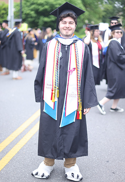 A student in cap and gown also sports the feet from the costume for school mascot, Rooney, a hawk