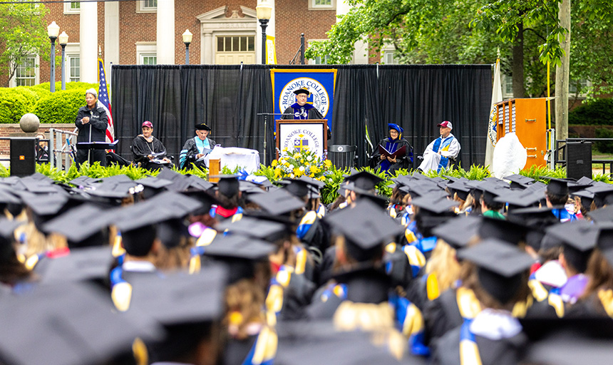 President Shushok speaks from the stage while looking out over a sea of students in caps and gowns