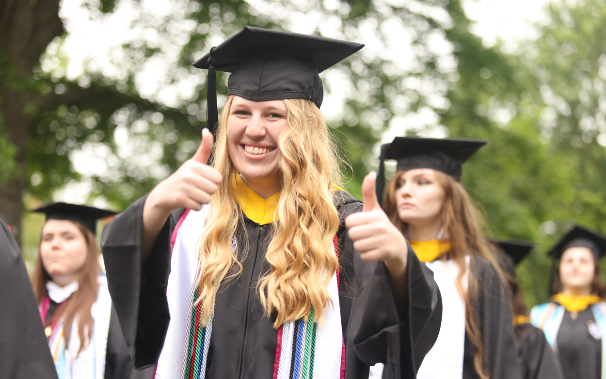 A student smiles and gives thumbs up to the camera while walking in the starting procession