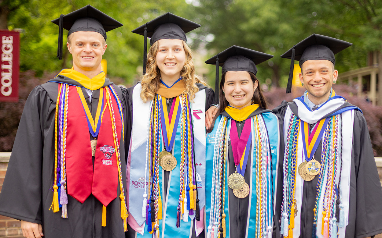 Four students in academic robes and regalia smile for a group photo