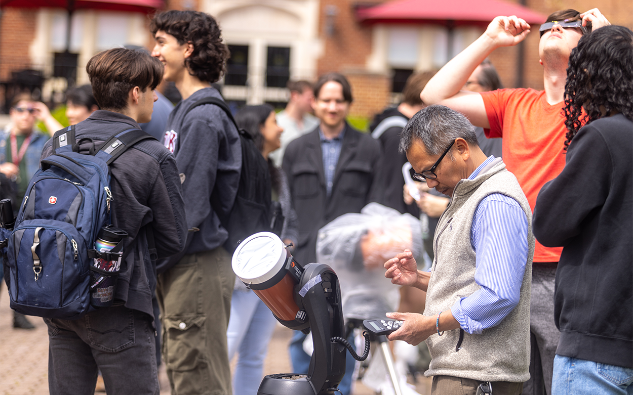 Truong Le adjusts telescope with crowd behind him. 