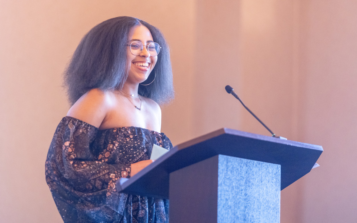 A student smiles while on stage at a podium