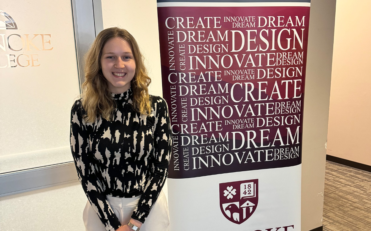 Student smiling next to a sign imprinted with words like: Create. Dream. Innovate.