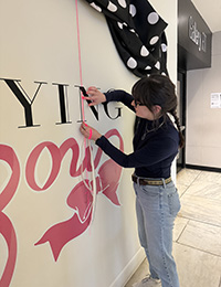 Bella Moritz measures the sign she is making on the wall for an exhibition called Untying the Bow.