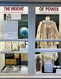 An exhibition behind glass shows recreated Sumerian funeral attire made of multicolored beads. Title of exhibit is "The Weight of Power."