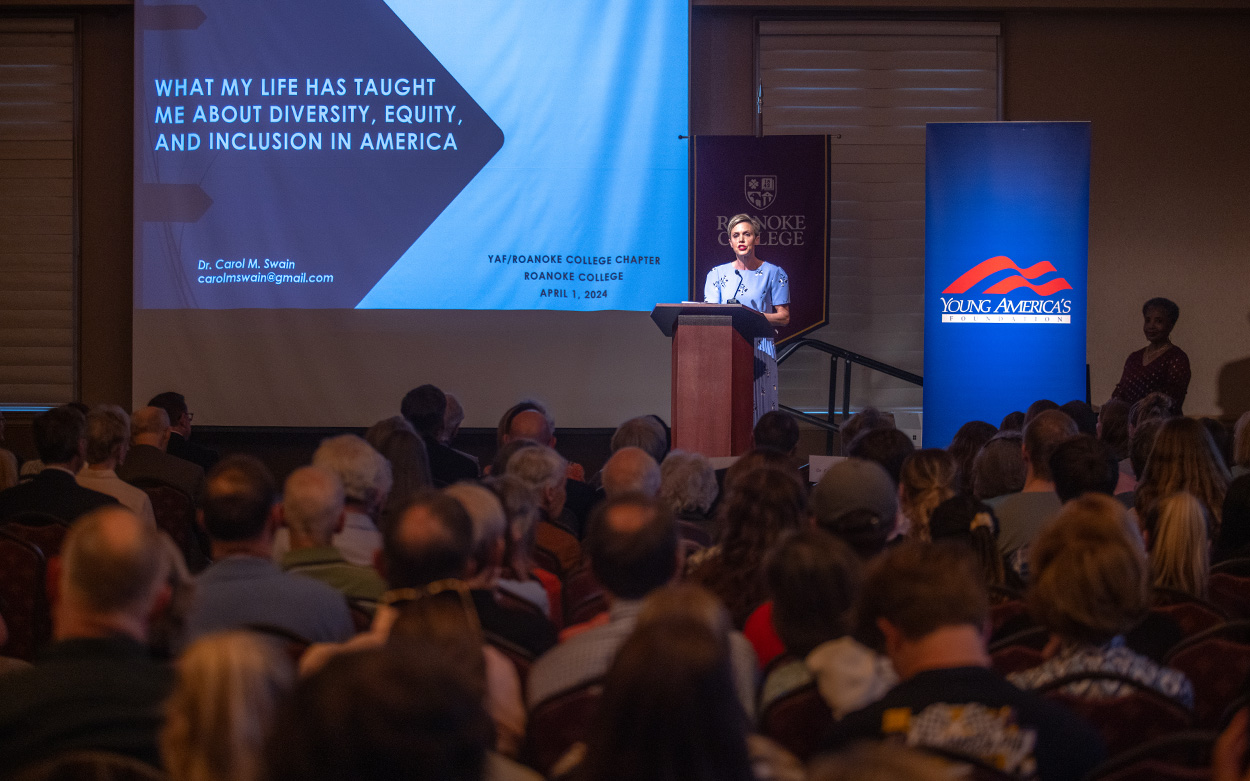 From a dais, Dr. Alice Kassens addresses a crowded audience in Roanoke College's Wortmann Ballroom