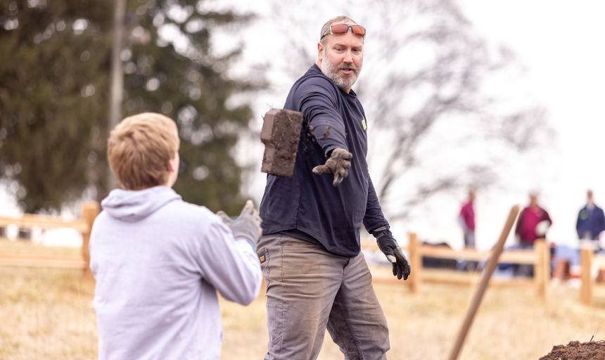 Adult passing a brick to a student worker during a outdoor project.