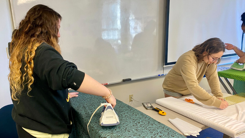 Student volunteers ironing and measuring fabric for Days for Girls supplies