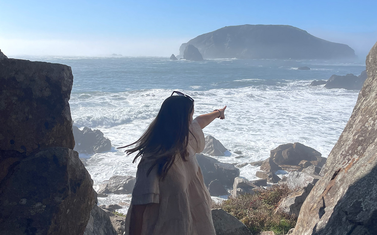 Kendall Donna turning and pointing at a scenic coastal overlook