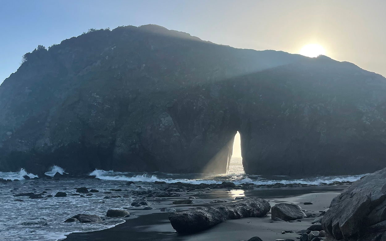 Sunlight shining through an opening in a large, coastal rock formation