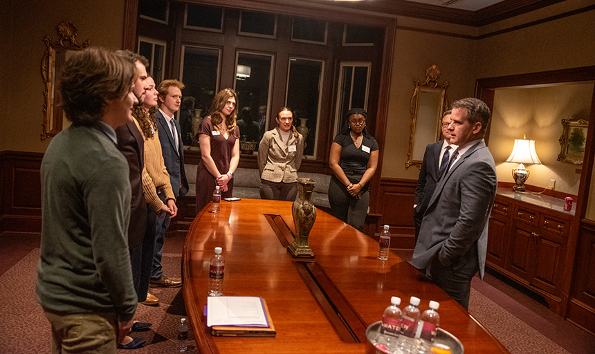 Adam Kinzinger, wearing a gray suit, talks to a half-circle of students in the president's dining room.