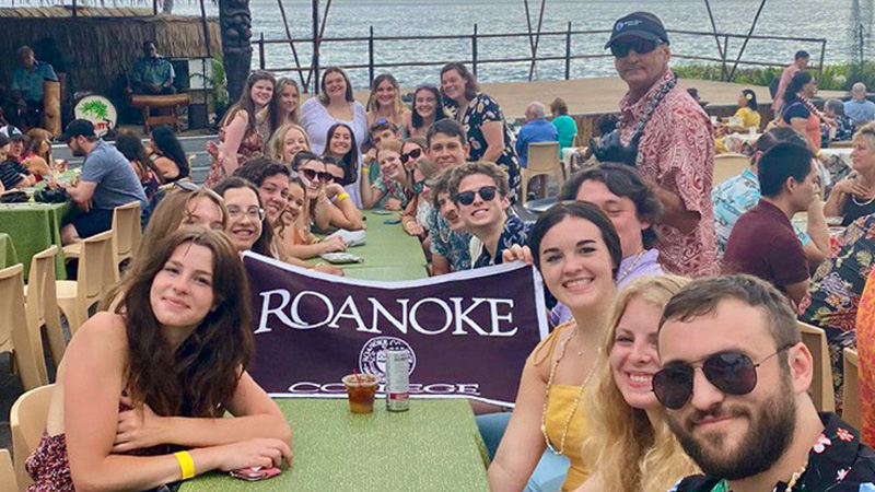 People smiling for a photo with a Roanoke College flag