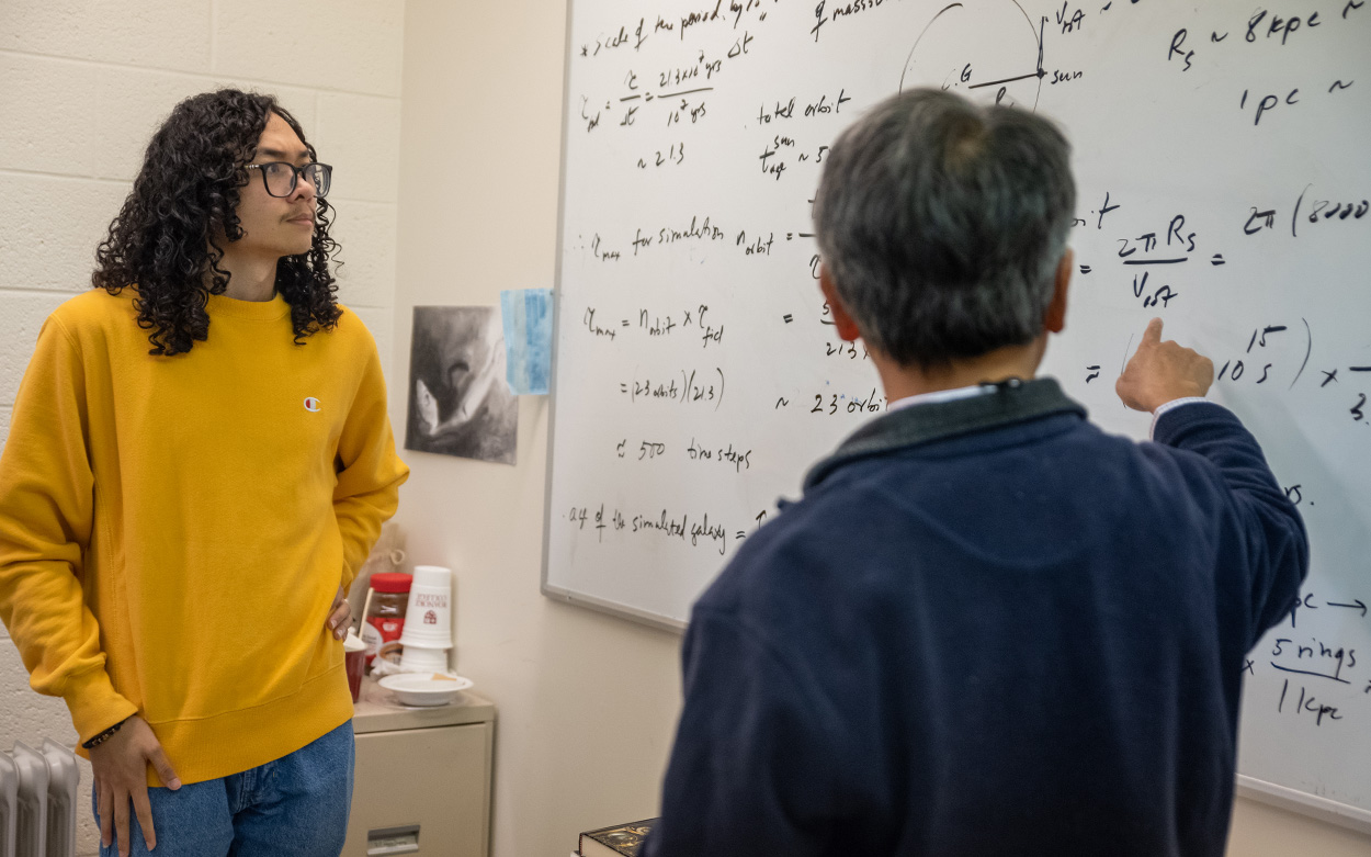 A student furrows his brow as a professor points to a whiteboard filled with mathematical calculations