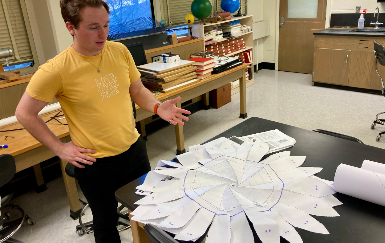 A student gestures while talking over a paper model of a starshade