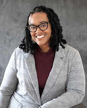 Head shot of a woman in a maroon shirt with a gray sweater buttoned over it. 