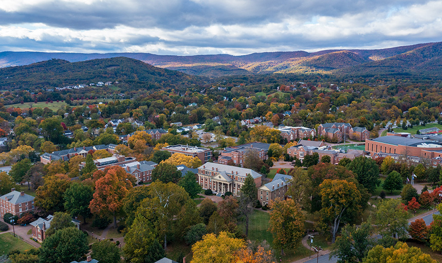 Aerial photo of red brick buildings among trees and purple mountain range in the distance
