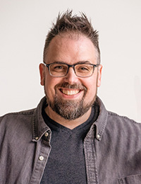 Headshot of a man in a gray shirt and glasses