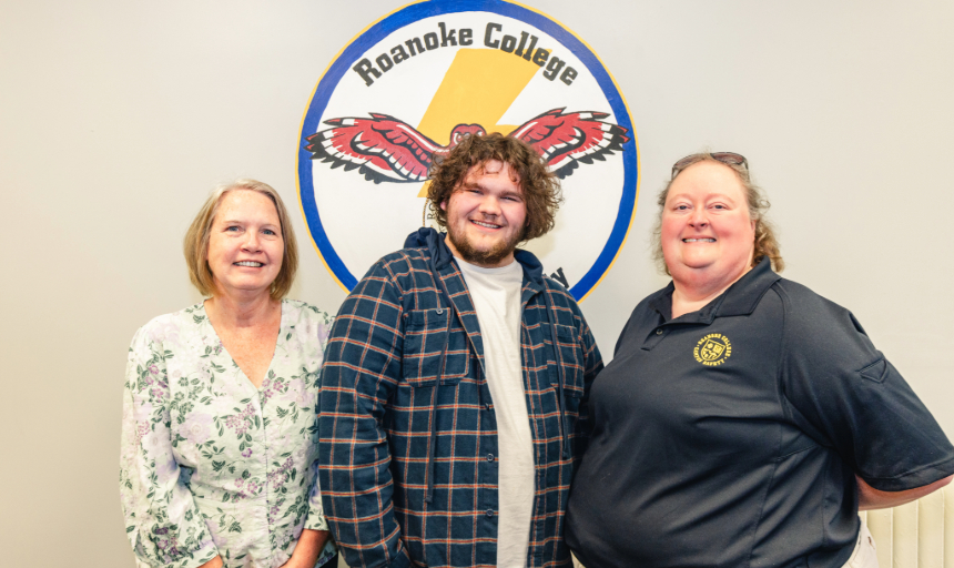 Karen Booth, Joseph Mills, Colin Waller and Mary Jones stand in front of the Roanoke College Campus Safety seal - a maroon bird flying in front of a lightning bolt, carrying the Roanoke College seal with its feet.