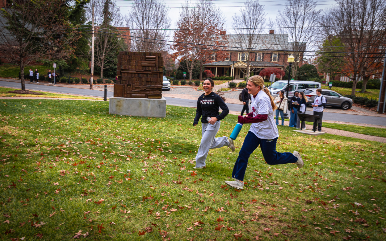 Students run in the grass in front of the Authors and Architects memorial on campus. 