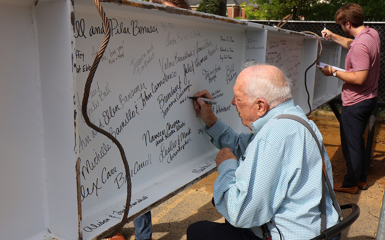 Two people sign a steel beam with markers