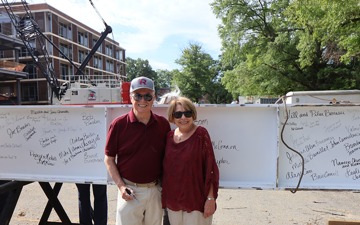 A couple smiles for a photo next to a large steel beam