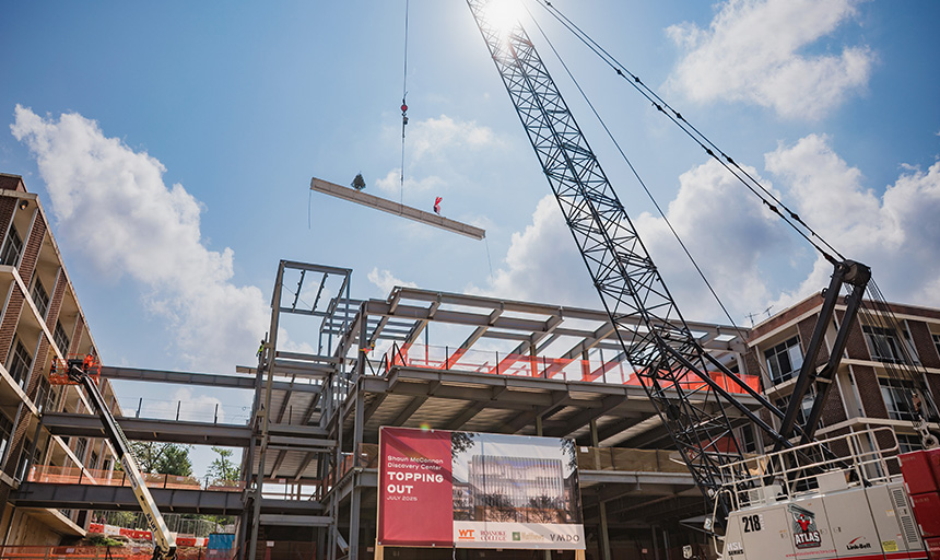 A crane lifts a steel beam high in the air over a construction site.