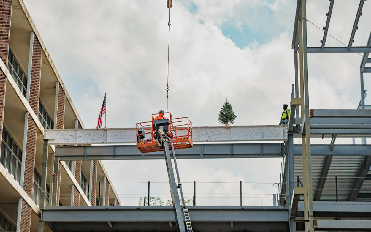 A construction worker on a lift affixes a steel beam into place