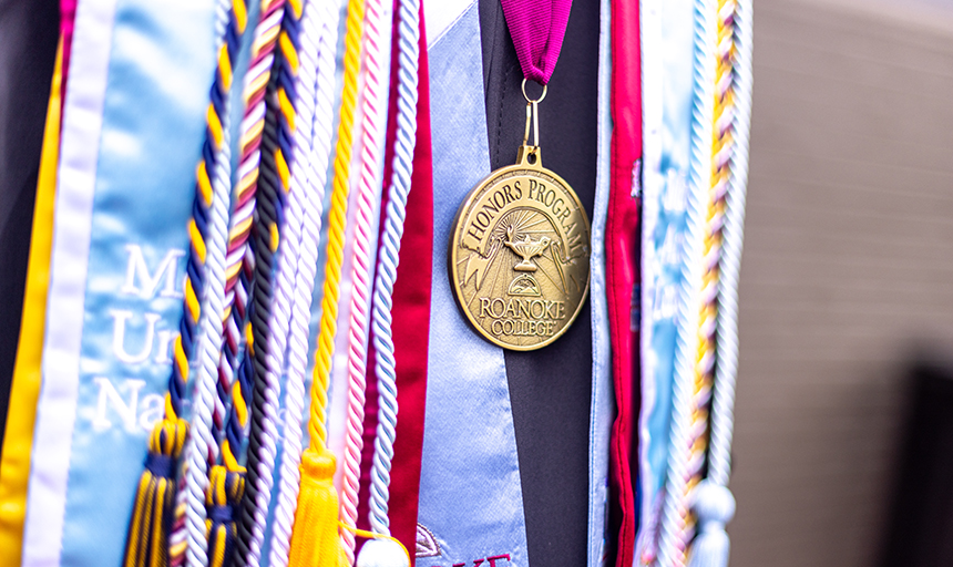 Detail shot of a gold "Honors Program" medal among various colored graduation sashes and cords