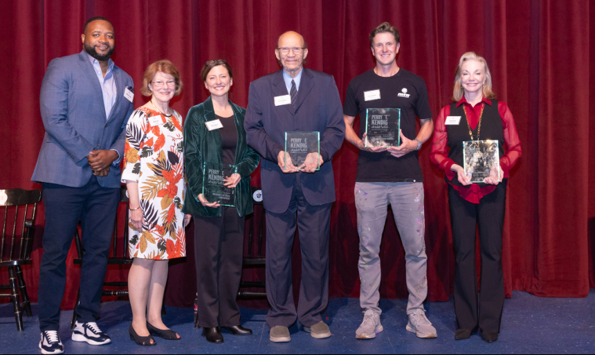 Recipients of the 2025 Perry F. Kendig Awards stand in front of a red curtain on stage, holding their awards. 