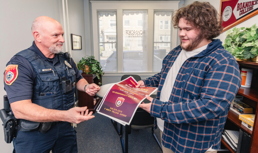 Student Colin Waller hands Campus Safety Officer Kenneth Assenat a stack of Campus Safety fliers.