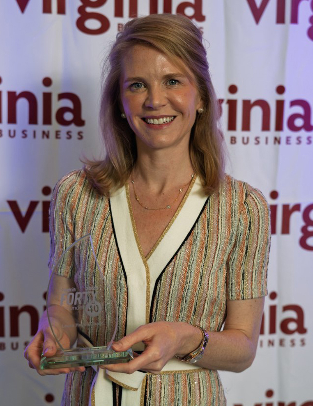 Woman holds an acrylic award shaped like a flame in front of a white backdrop with "Virginia Business" on it.