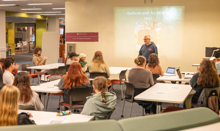 Associate Professor Robert Willingham speaks to a group of students in the Fintel Library during a coffee shop talk on memorials. A photo of the "Authors and Architects" memorial is projected onto the wall behind him.