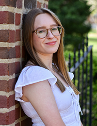 Portrait of a brown-haired young woman wearing glasses and a white dress.