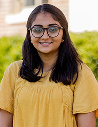 Headshot of young lady with black hair and glasses wearing a yellow shirt.