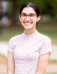 Headshot of young woman with black hair and glasses wearing white top with red flower print