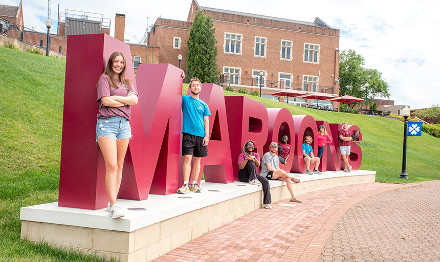 Several students pose, sitting or standing, among six-foot maroon letters that spell out "Maroons."