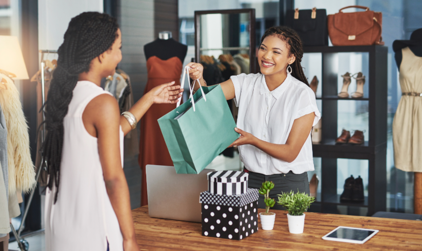 A store clerk smiling while handing a customer her purchases