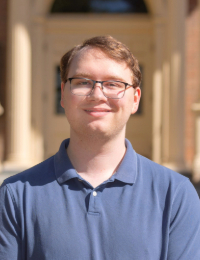 Headshot of young man with brown hair and glasses in blue polo shirt