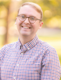 Headshot of a man in a pink dress shirt.