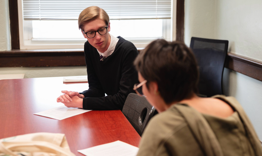 Two students leaning in and talking at a table
