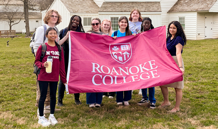 A group of students from the H2O living-learning community stand in front of LewisGale Hospital Alleghany and hold up a maroon-colored Roanoke College flag. 