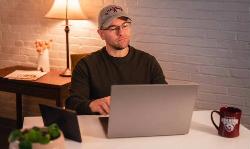 A man sits at his desk working on his laptop. 