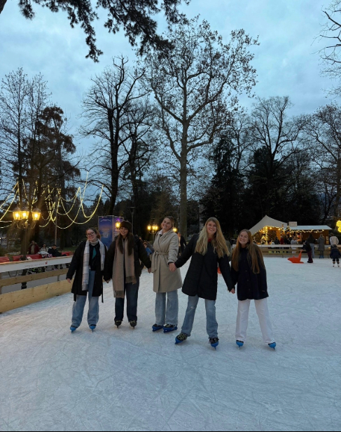 Five women hold hands while ice skating in an outdoor rink in Lugano. 