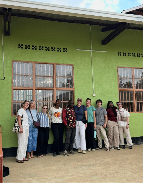 A group of people, most of them from the Linking Lives program, stand together outside a green building in Rwanda. 