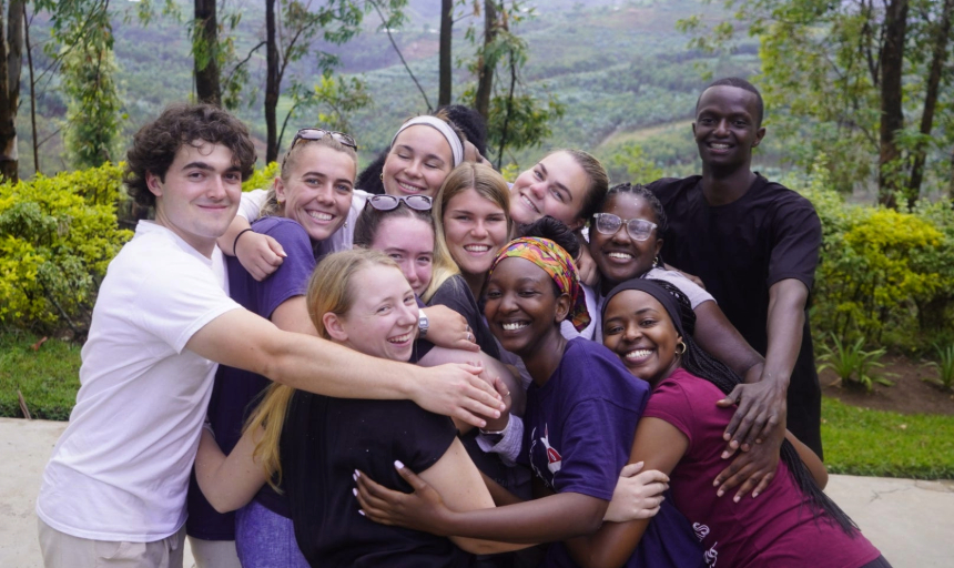 A group of people hug in Rwanda hug and smile at the camera. 